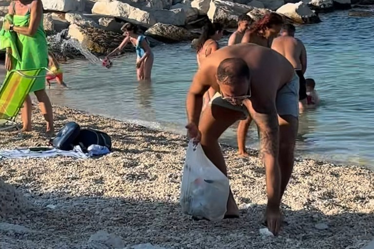 Turista francese raccoglie rifiuti alla spiaggia